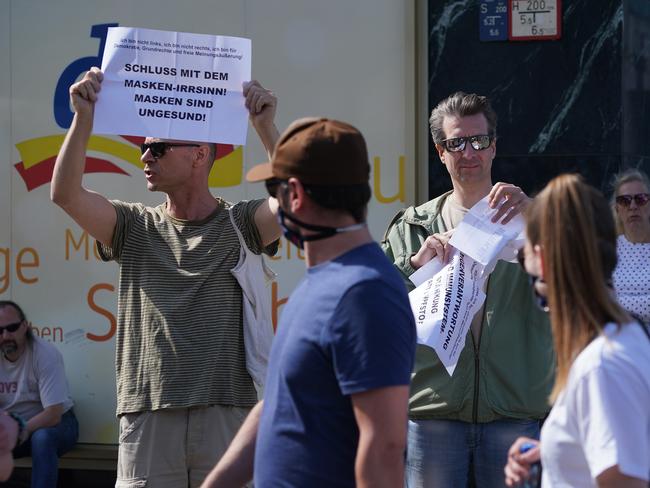 People wearing protective face masks walk past a man holding a sign that reads: "Enough of the mask craziness! Masks are unhealthy!" in Berlin. Picture: Getty Images