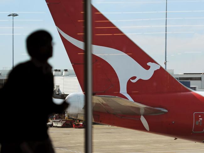 (FILES) This file picture taken on August 22, 2012 shows an airport passenger walking inside a terminal past the tail of a Qantas plane at the Sydney International Airport. - Australian flag carrier Qantas on August 20, 2020 posted an almost 2 billion USD annual loss after a "near-total collapse" in demand due to the COVID-19 coronavirus pandemic. (Photo by Greg WOOD / AFP)