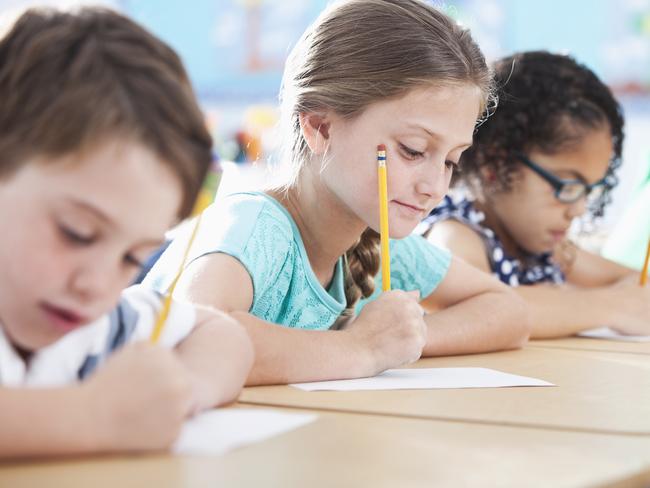 Multi-ethnic elementary school children writing in classroom.  Focus on girl in light blue shirt (10 years).