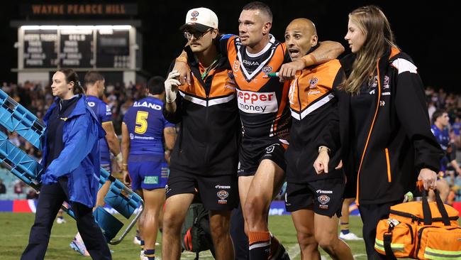 Brent Naden of the Wests Tigers is assisted off the field after a knee injury. (Photo by Mark Metcalfe/Getty Images)