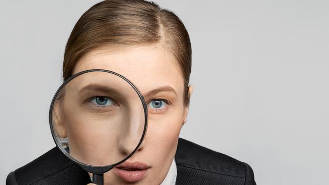 Portrait of a girl in the office at work looks carefully into the magnifying glass with one eye. The concept of office work and search. tax generic