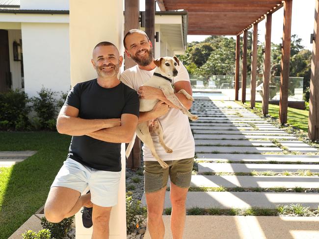 18/9/2019 : Interior designers Gavin Atkins and  Warren Sonin (in white T) holding Charlie the dog  (Gav and Waz), at their home at Cooroy on the Sunshine Coast. The pair were on the first series of reality renovation show The Block in 2003 and have transformed their Cooroy Mountain property into a luxury lodge. Lyndon Mechielsen/The Australian