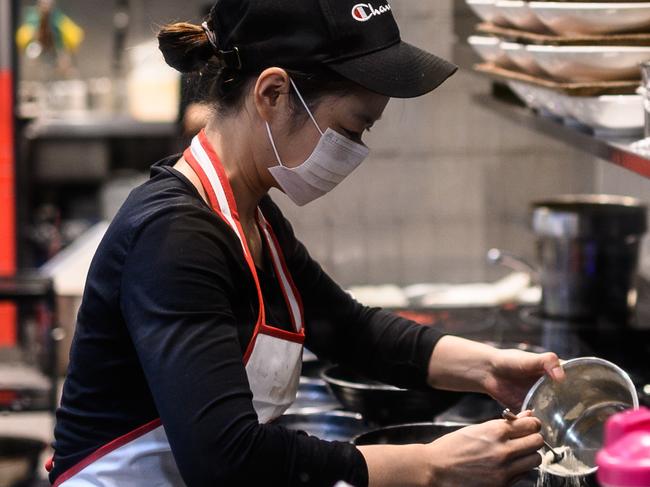 A woman seen wearing a protective face mask in a restaurant kitchen in Sydney, Monday, March 16, 2020. (AAP Image/James Gourley) NO ARCHIVING