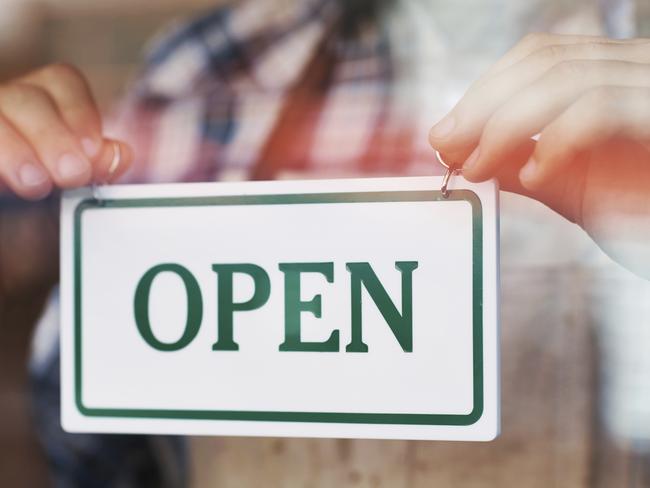 Close up shot of person holding an 'OPEN' sign against the class of the cafe door. Free to use from iStock