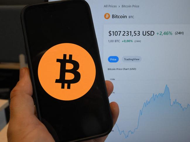 This illustration photograph shows the Bitcoin cryptocurrency logo displayed on a smartphone beside a screen showing a trading chart in Brussels on December 17, 2024, (Photo by Nicolas TUCAT / AFP)