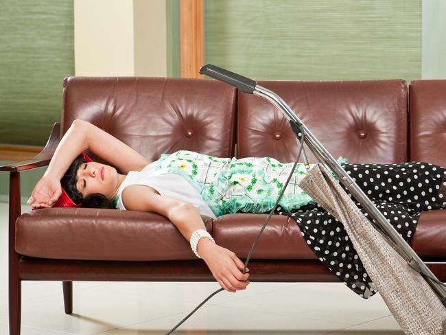 1950's housewife  with apron, napping on mid-sentury modern couch with Retro Hoover vacume cleaner