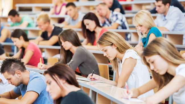 "Group of college students in the university amphitheatre, they are sitting and doing an exam."