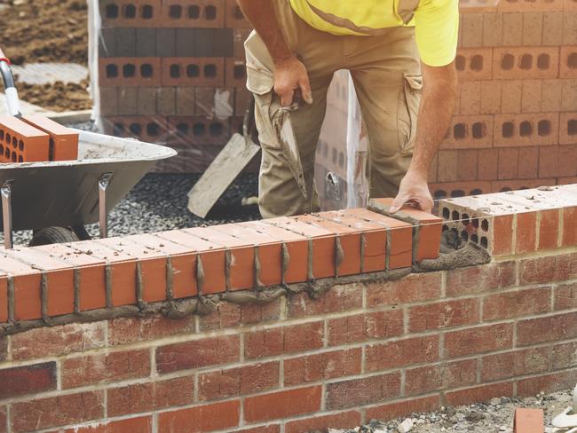 Developing Queensland - Industrial bricklayer laying bricks on cement mix on construction site.