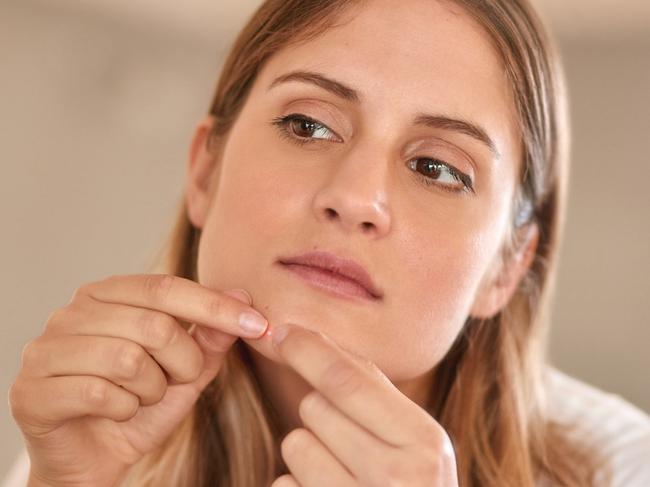 Cropped shot of a young woman squeezing a pimple on her face