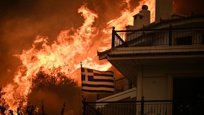 A Greek flag flies during a wildfire on the outskirts of Athens in August. Picture: Angelos Tzortzinis / AFP