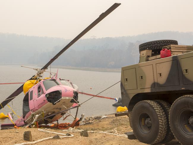 An Australian Army Heavy Recovery Vehicle is used to successfully recover an NSW RFS contracted helicopter that ditched into the Ben Boyd Reservoir, near Eden in NSW. *** Local Caption *** The Australian Defence Force (ADF) has commenced Operation Bushfire Assist 19-20 and has stood up Joint Task Forces (JTF) in New South Wales and Victoria to enhance Defence support following devastating bushfires in the South East of Australia. ADF members are working side by side with emergency services personnel in the State Disaster Coordination Centre (SDCC) of the NSW Rural Fire Service Headquarters and alongside the Victorian Country Fire Service and Metropolitan Fire Brigades to provide best effect of ADF assets.  On Sunday 12 January, Fire and Rescue NSW and members of the Australian Defence Force successfully retrieved a helicopter that was forced to ditched into the Ben Boyd Reservoir, near the township of Eden on Thursday 9 January. The Bell UH-1H was contracted to the NSW Rural Fire Service and was supporting the firefighting efforts of the Clyde Mountain fire at the time.  The retrieval mission saw Royal Australian Navy, Clearance Diving Team One and the Fire and Rescue NSW’s Hazardous Materials Team (HAZMAT) bring the helicopter to shore. Using floats secured by the Navy clearance diving team, the helicopter was floated approximately 400 metres to the shoreline and was held within containment and absorbent booms to alleviate potential water contamination.  The Bell UH-1H was then brought onto the shore by an Australian Army Heavy Recovery Vehicle operated by 5 CSSB and was handed over to the relevant authorities.