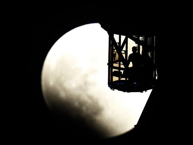 The Earth’s shadow renders the moon as a couple in Ferris wheel observe it during a total lunar eclipse in Tokyo. Picture: AP