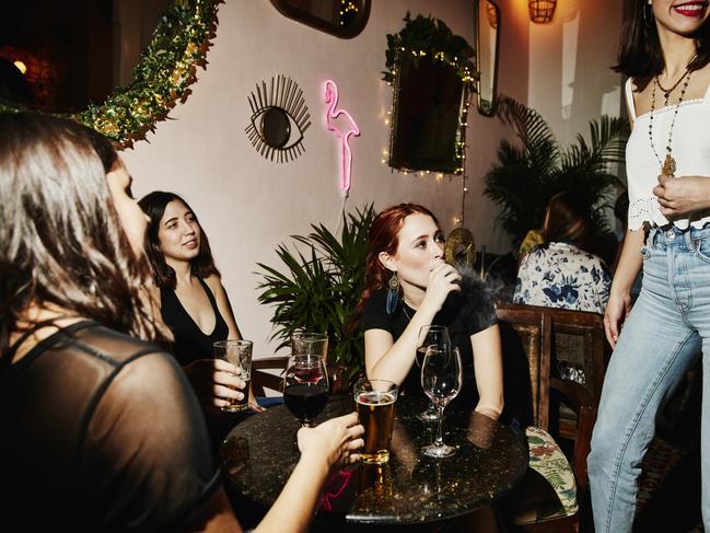 Woman smoking electronic cigarette while hanging out with friends in night club