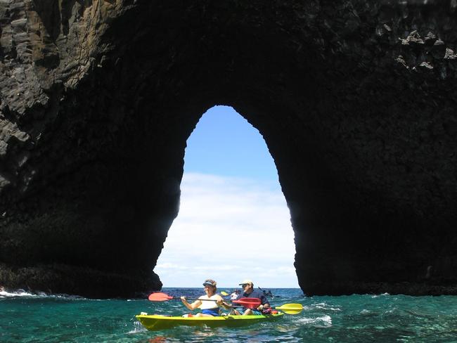 Tourists paddle through “The Arch” in the South Pacific seas off the island.