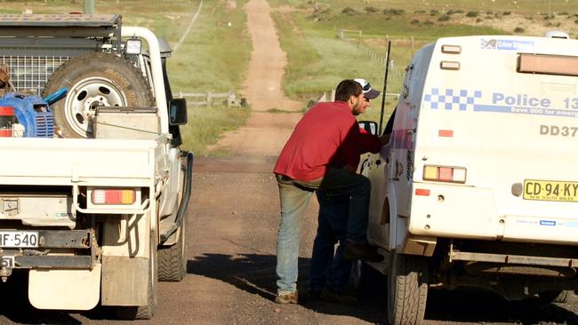 Max McKenzie (no hat) from a neighbouring property speaks to police during the operation. Picture: Neil Keene