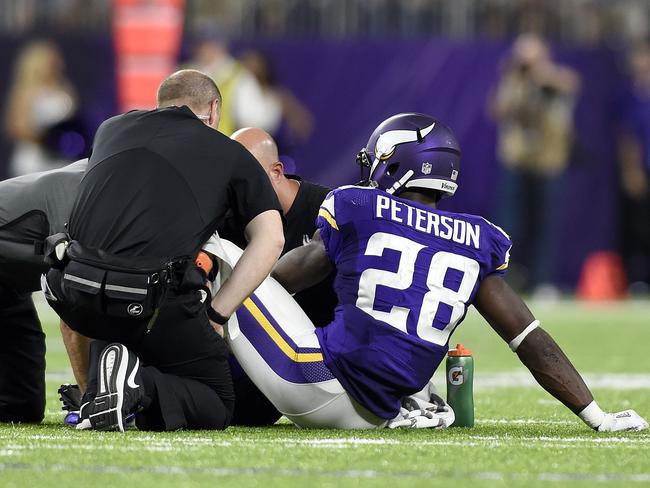 Adrian Peterson #28 of the Minnesota Vikings sits on the field as trainers tend to his knee.