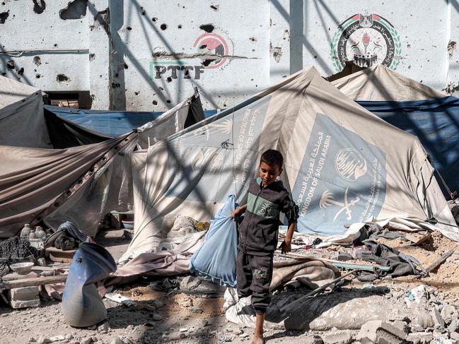 A boy walks with a pillow past a tent shelter in the yard of the Shuhada (Martyrs) school, which was hit by Israeli bombardment, in Nuseirat in the central Gaza Strip on October 24, 2024 amid the ongoing war in the Palestinian territory between Israel and Hamas. (Photo by Eyad BABA / AFP)