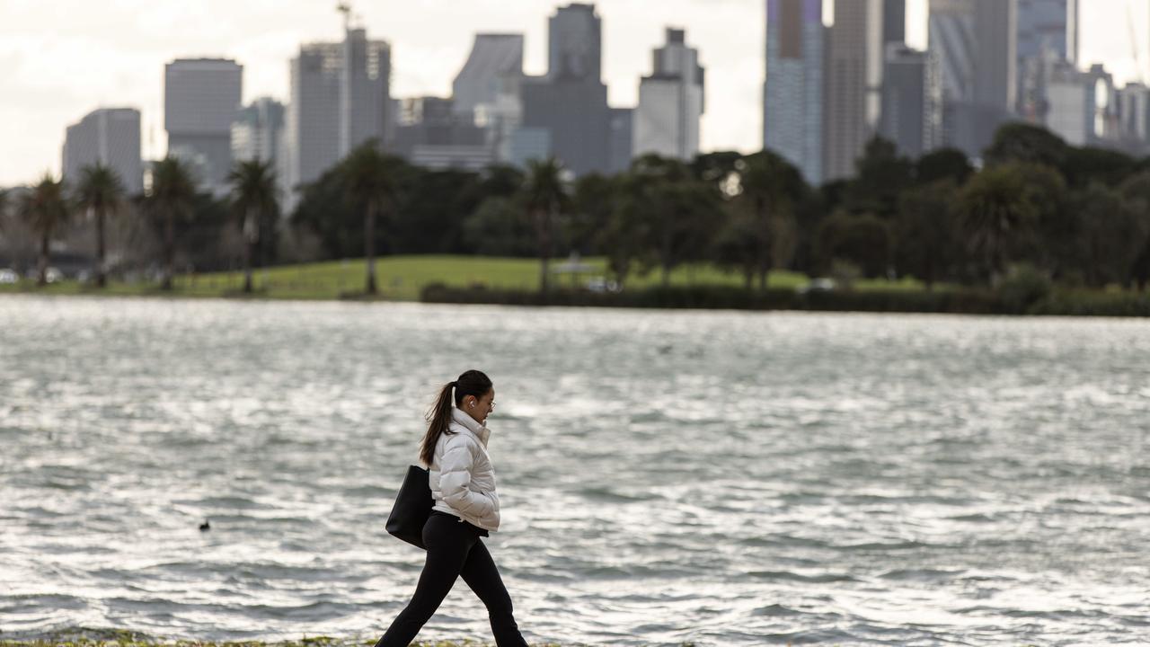 Clouds above the Melbourne skyline as a person walks through Albert Park.