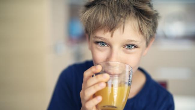 Portrait of a cute little boy aged 9 drinking a glass of orange juice Nikon D850