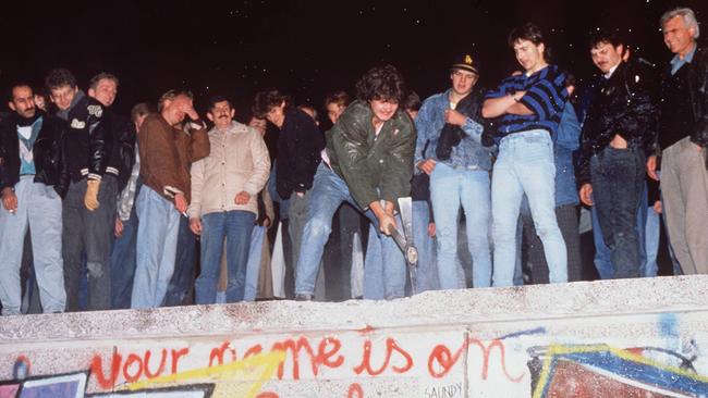 As the Berlin Wall comes down, people celebrate as workers dismantle the wall.