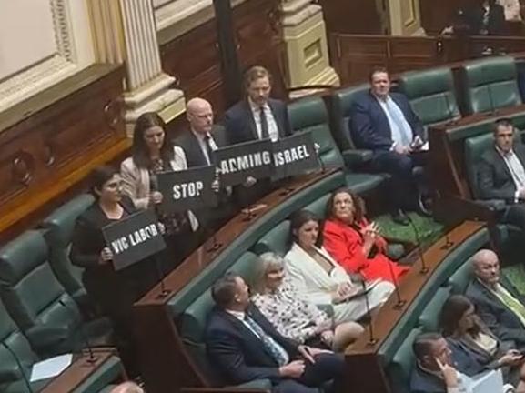 Greens MPs holding up signs which read: 'Vic Labor stop arming Israel'.