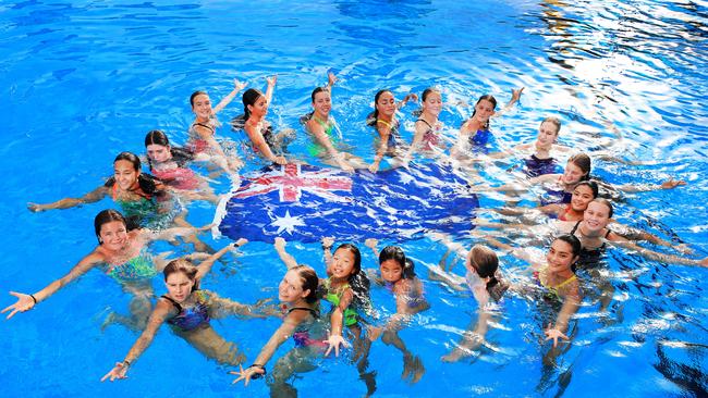 The Gold Coast Mermaids synchronised swim team get into the Australia Day spirit at Gold Coast Aquatic Centre while Angus Cope and Cameron Medley watch on from the pool. Picture: Scott Powick