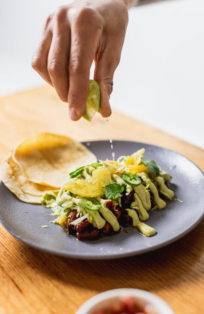 A Pork Carnitas dish consisting of pork belly pieces, smoked pineapple, adobo sauce, avocado crema, pickled pineapple , lettuce, green chilli, lime, soft corn tortillas