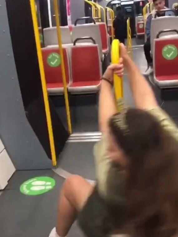 A girl dances using one of the handles on a train.