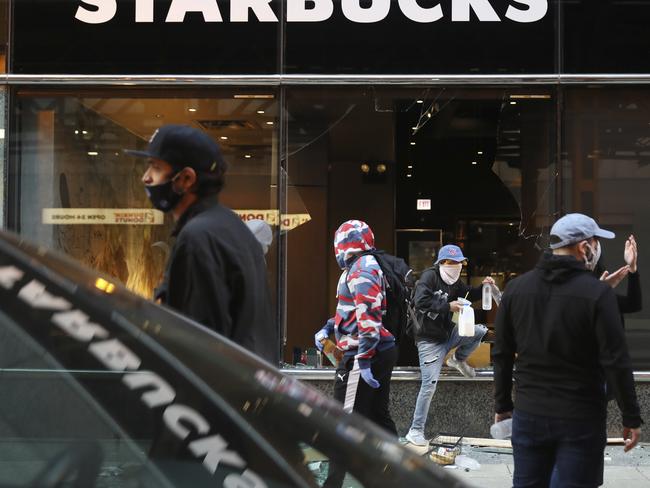 A person exits a broken window of a Starbucks, in Chicago, carrying items after a march and rally over the death of George Floyd. Picture: John J. Kim/Chicago Tribune via AP