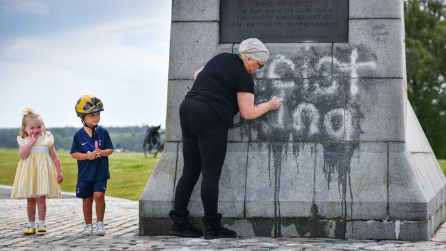 Children look on as a member of the public cleans the Robert the Bruce Statue which was defaced with graffiti in Bannockburn, Scotland.