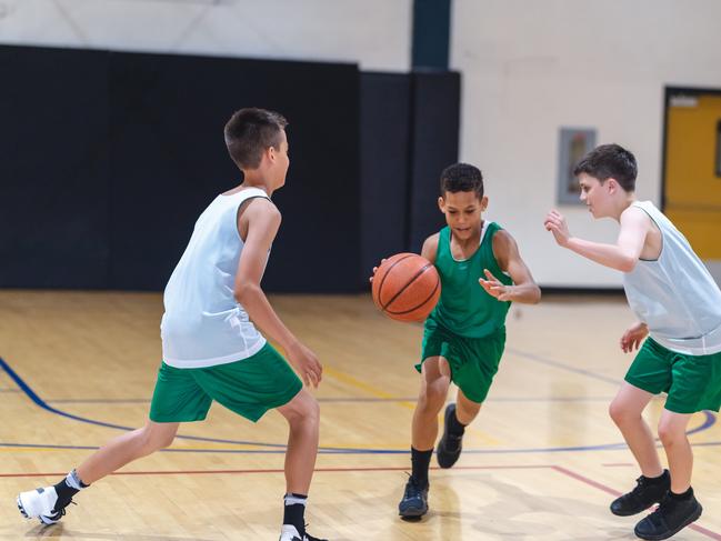 A young African American boy dribbles through two defenders and tries to score. istock image