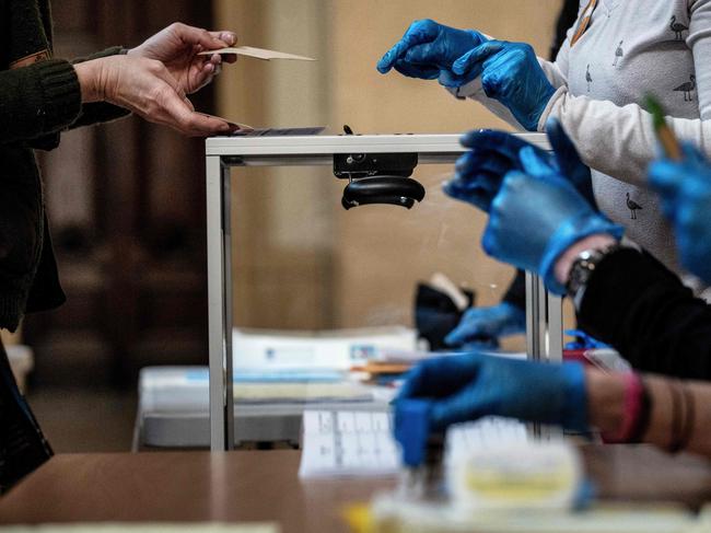 A voter casts their ballot in front of an official wearing plastic gloves in a polling station of Lyon during the first round of the mayoral elections. Picture: AFP