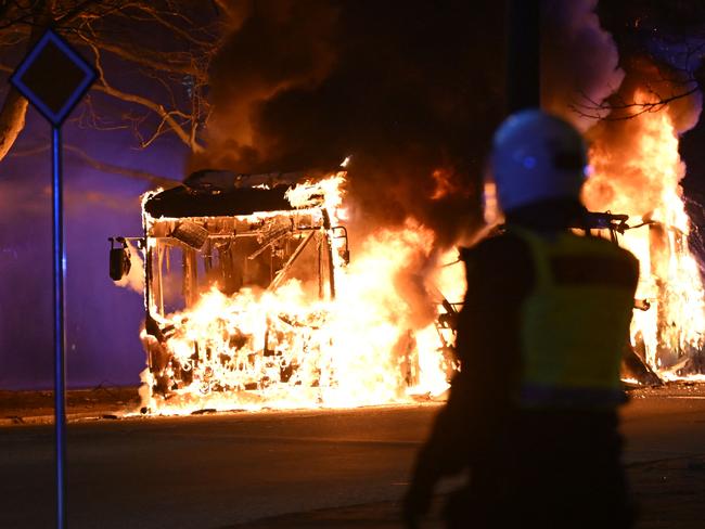 TOPSHOT - An anti-riot police officer stands next to a city bus burning in Malmo late April 16, 2022. - The unrest in Malmo has continued after Rasmus Paludan, party leader of the Danish right-wing extremist party Tight Course, held a demonstration on April 16, 2022 at Skanegarden near the Oresund Bridge. (Photo by Johan NILSSON / TT NEWS AGENCY / AFP) / Sweden OUT