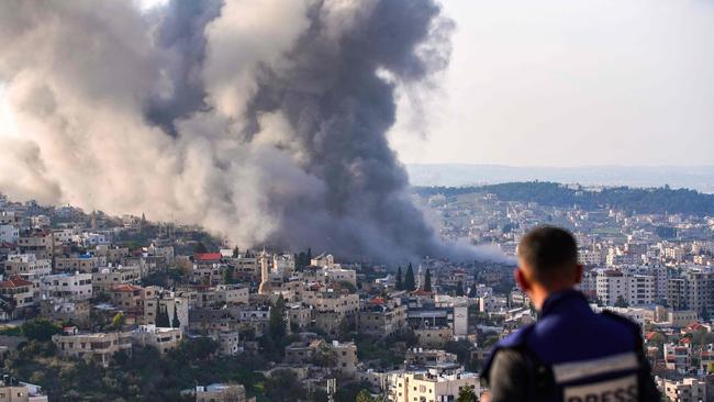 A journalist looks on as smoke billows from the site of several explosions during an Israeli raid in Jenin. Picture: AFP.