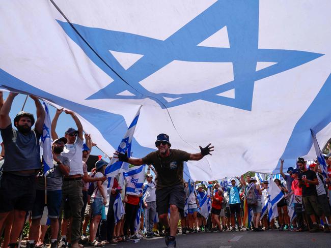 Protesters lift a large national flag during a demonstration near the Knesset, Israel's parliament, in Jerusalem on July 24, 2023, amid a months-long wave of protests against the government's planned judicial overhaul. Israeli lawmakers on July 24 prepared for a final vote on a major component of the hard-right government's controversial judicial reforms even as US President Joe Biden called for postponing the "divisive" bill that has triggered mass protests. (Photo by Menahem KAHANA / AFP)