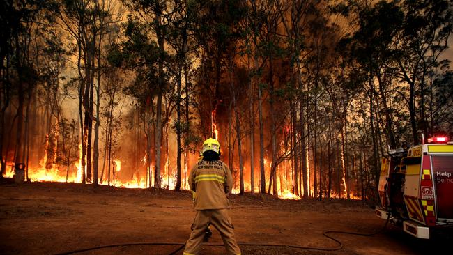 Firefighters hold back a fire threatening a house on The Buckets Way at Tinonee near Taree. Picture Nathan Edwards.