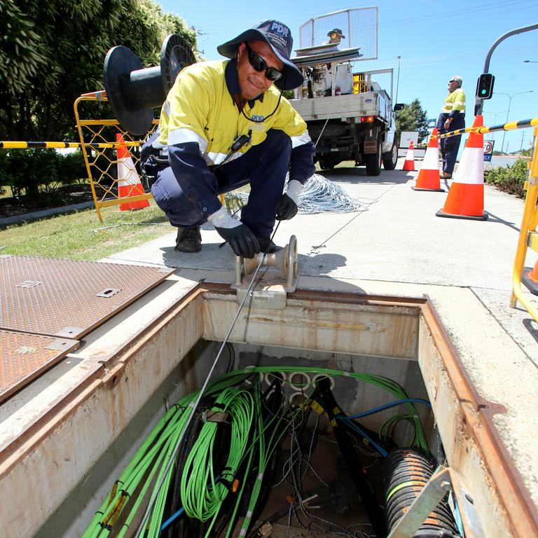 An NBN worker installing fibre cables in a street side pit.