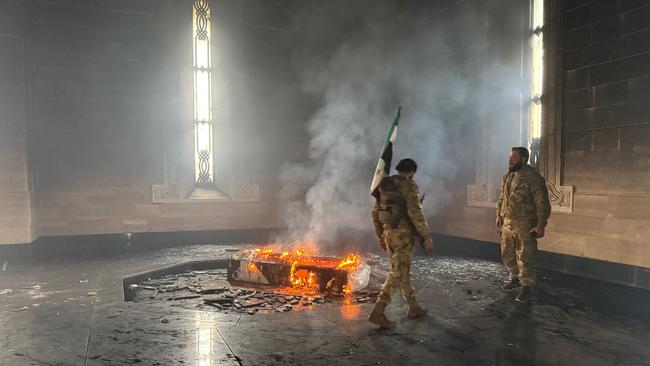 Rebel fighters stand next to the burning gravesite of Syria's late president Hafez al-Assad at his mausoleum in the family's ancestral village of Qardaha in the western Latakia province. Picture: AFP