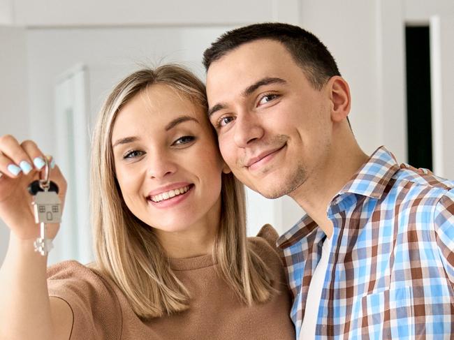 FIRST HOME BUYER Happy young couple home owners holding keys in new home. Smiling independent millennial man and woman first time homeowners carrying boxes on moving day. Mortgage loan, new house ownership concept.