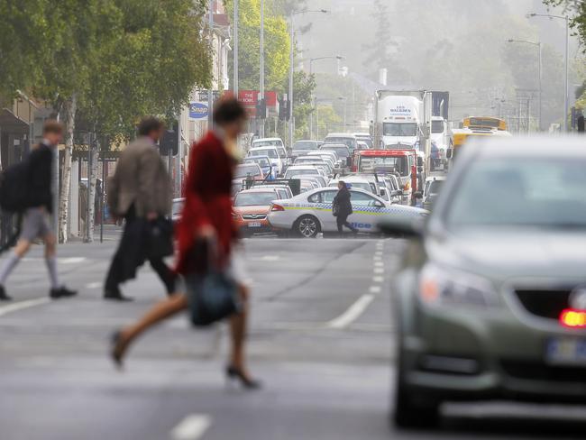 Pedestrians walk across the closed section of Macquarie St in Hobart after a part of Hadleys Hotel roof being ripped off.