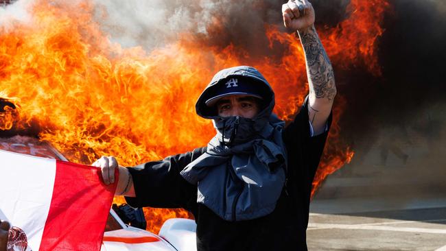A protester raises their fist while holding a Mexican flag in front of a Waymo vehicle that was set on fire during the Los Angeles protests. Picture: AFP.