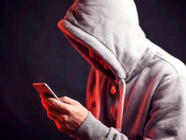 Man wearing hoody sweater with mobile phone in hands. Crime and hacking concept; scam generic.