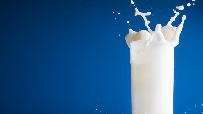 Milk splash in glass on blue background. Istock