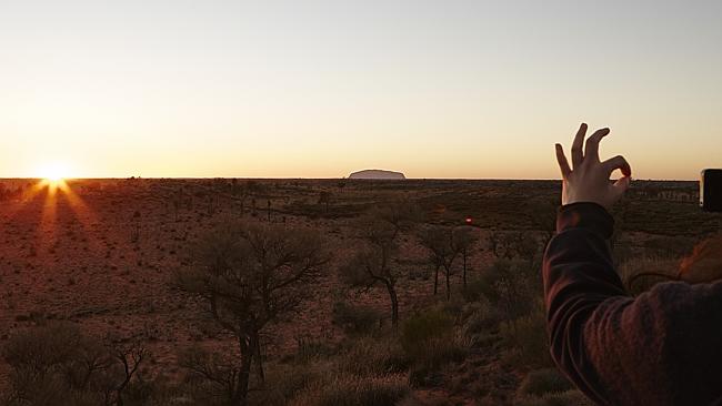   A tourist takes a photo of sunrise and Uluru, from the Olgas viewing platform. Picture: Lisa Perkovic 