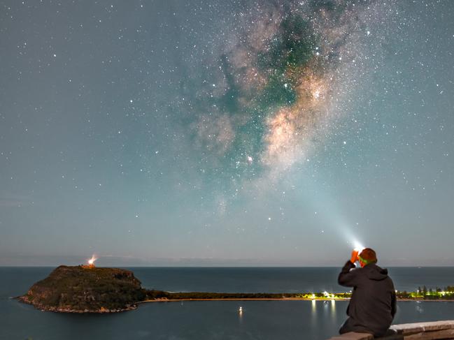 A man sitting at West Head lookout looking up to the Milky Way with the Barrenjoey Headland in the background. Picture: Greg Barber