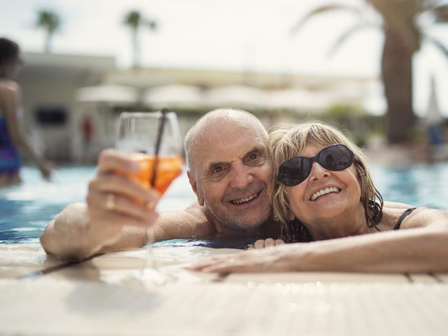 Happy senior couple enjoying summer vacations. The couple is enjoying a cocktail drink in the swimming pool. Retirees retirement generic.