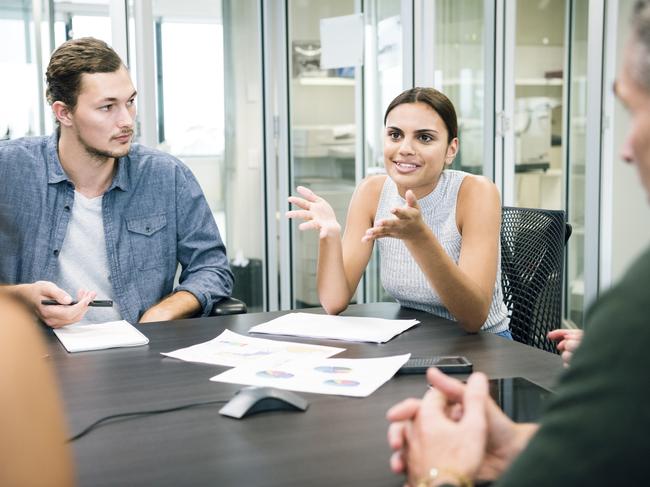 Young ethnic aboriginal Australian businesswoman in meeting with business colleagues she is talking and gesturing with hands in discussion around a table in a modern Sydney office.