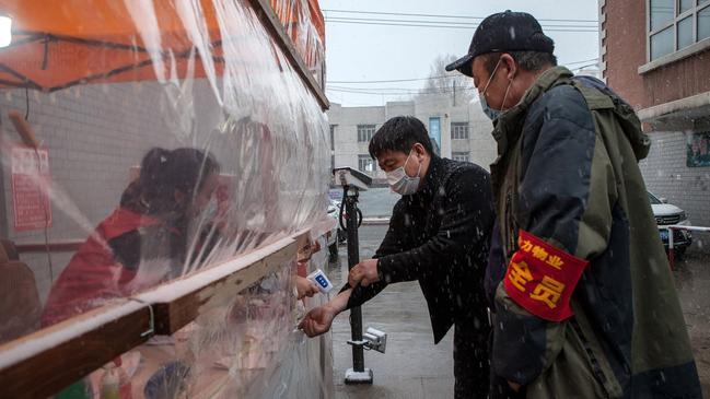 A man’s body temperature is checked before he can enter a community in the border city of Suifenhe, China, where new clusters of coronavirus have forced officials to tighten restrictions on movement. Picture: AFP