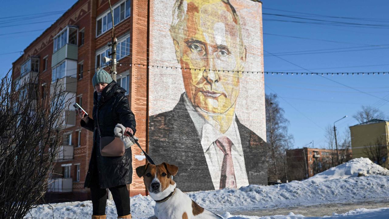 A woman walks her dog as she passes by a mural of Russian President Vladimir Putin in Kashira. Picture: Natalia KOLESNIKOVA/AFP