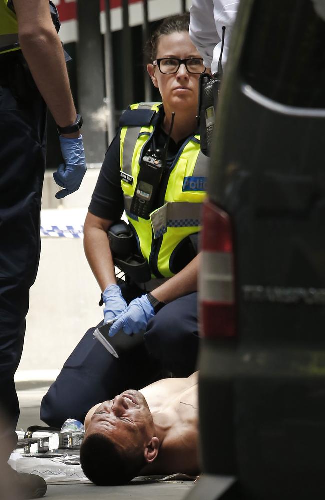 The alleged driver shot by police lies on the ground in pain guarded by police outside 535 Bourke Street. Picture: David Caird